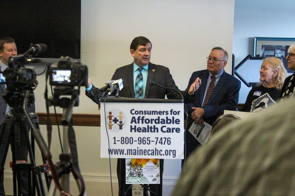 Troy at podium with sign reading "Consumers for Affordable Health Care"
